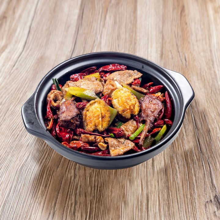 Dry hot pot of lamb/beef, abalone and dark red chillies in black serving bowl on wood background.