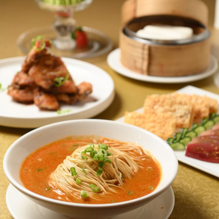 Traditional dan dan noodles in spicy soup in white bowl surrounded by side dishes and bamboo steamer basket.